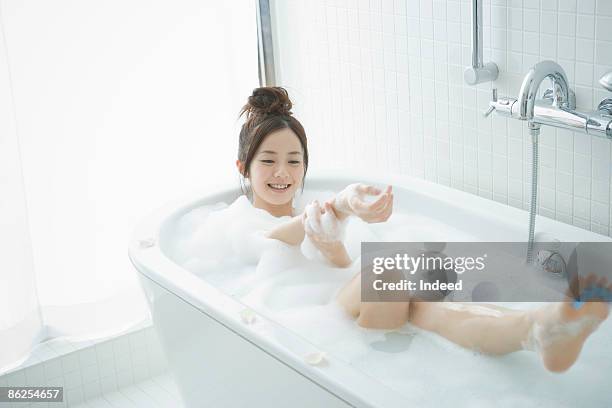 young woman in bubble bath, massaging her arm - japanese women bath stock pictures, royalty-free photos & images