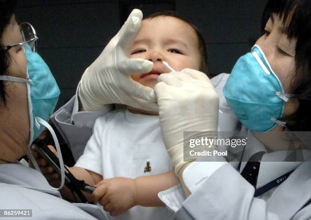 South Korean quarantine officers try to take samples from a baby who arrived from the US at Incheon International Airport on April 28, 2009 in...