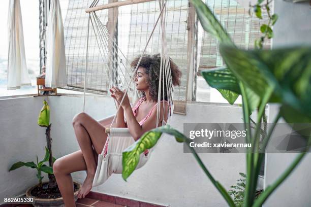 thoughtful young woman sitting on swing at home - caribbean dream stock pictures, royalty-free photos & images