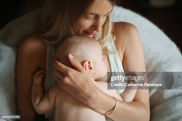 a 3 months old baby boy sleeping in the arms of his mum - mum sitting down with baby stockfoto's en -beelden