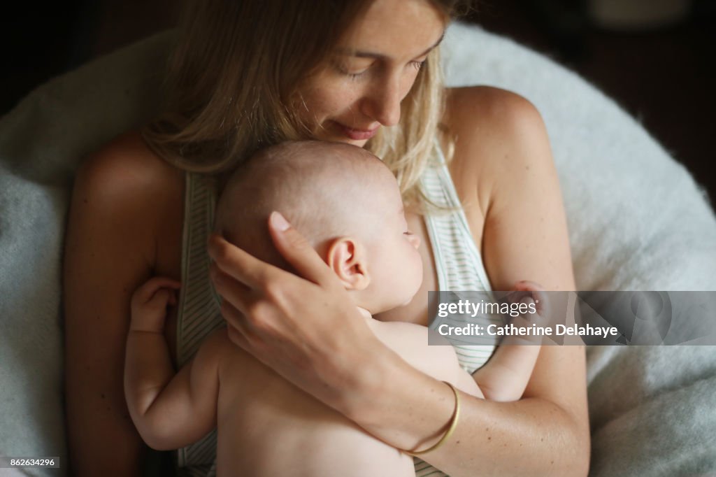 A 3 months old baby boy sleeping in the arms of his mum