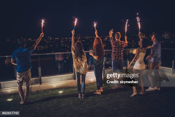 group of young adults having fun with sparklers on a penthouse balcony by night. - women of penthouse stock pictures, royalty-free photos & images