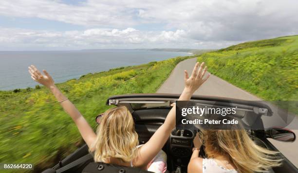 two women in car driving along coast road with roof down - blonde attraction stock pictures, royalty-free photos & images