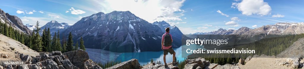 Panoramic of young man hiker on rock above mountain lake