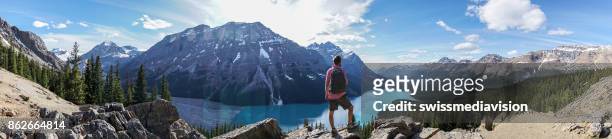 panoramic of young man hiker on rock above mountain lake - panoramic lake stock pictures, royalty-free photos & images