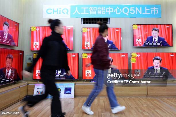 People walk past television screens showing China's President Xi Jinping as he delivers a speech during the opening of the 19th Communist Party...