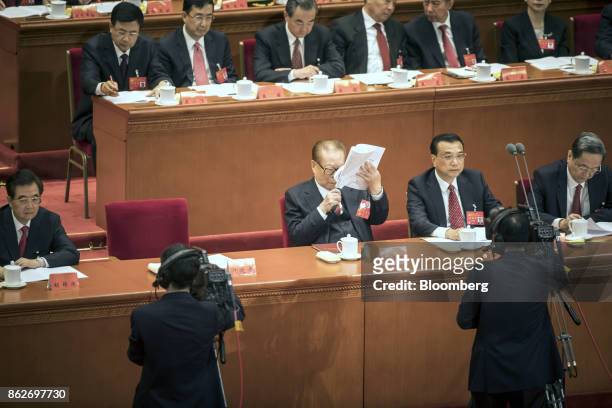 Jiang Zemin, China's former president, center, holds a magnifying glass while reading a report as he sits alongside Li Keqiang, China's premier,...