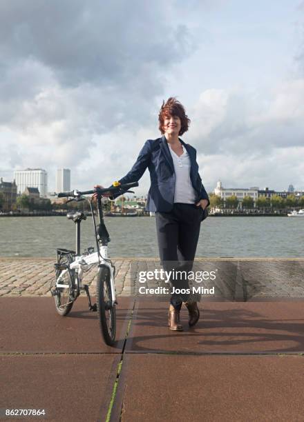 businesswoman with her folding bike, portrait - tossing hair facing camera woman outdoors stock-fotos und bilder