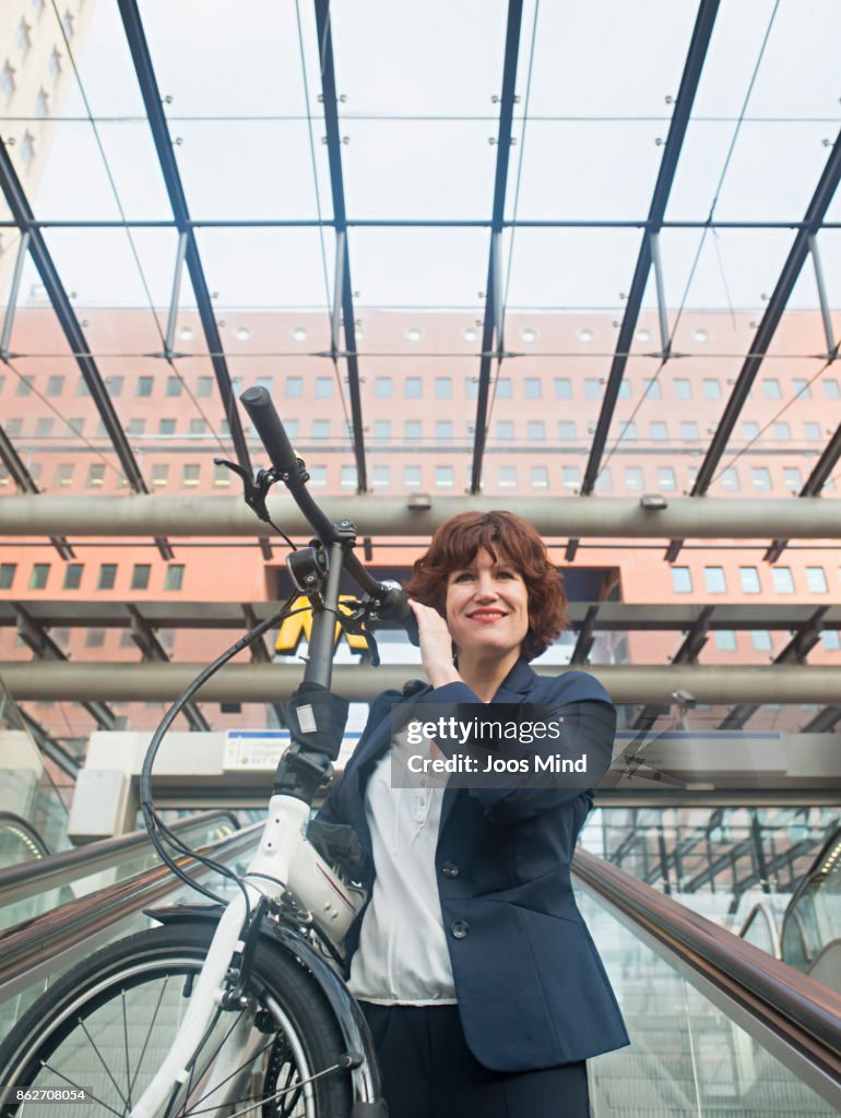 Businesswoman carrying bike on shoulder, using escalator to subway