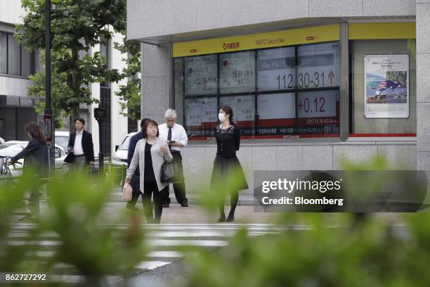 Pedestrians wait to cross a road in front of an electronic stock board outside a securities firm in Tokyo, Japan, on Wednesday, Oct. 18, 2017. As...