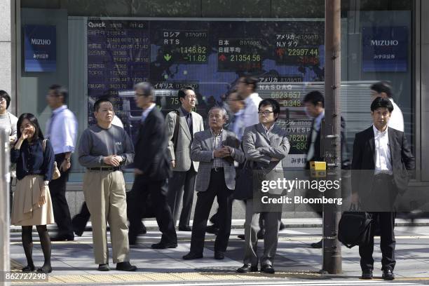 Pedestrians wait to cross a road in front of an electronic stock board outside a securities firm in Tokyo, Japan, on Wednesday, Oct. 18, 2017. As...