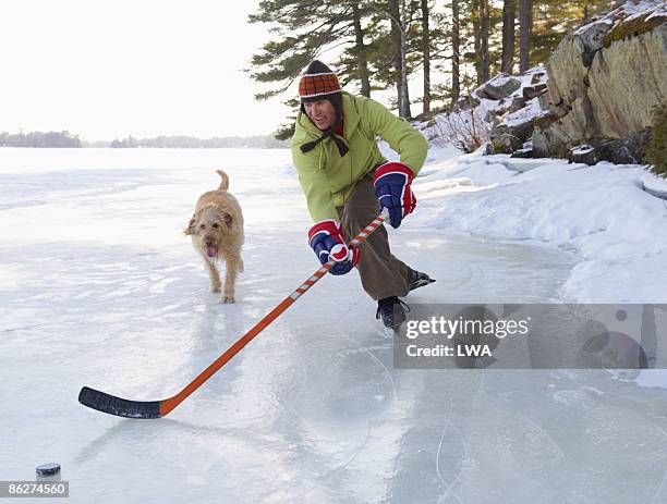 man playing hockey on frozen lake, dog beside him - mens ice hockey fotografías e imágenes de stock