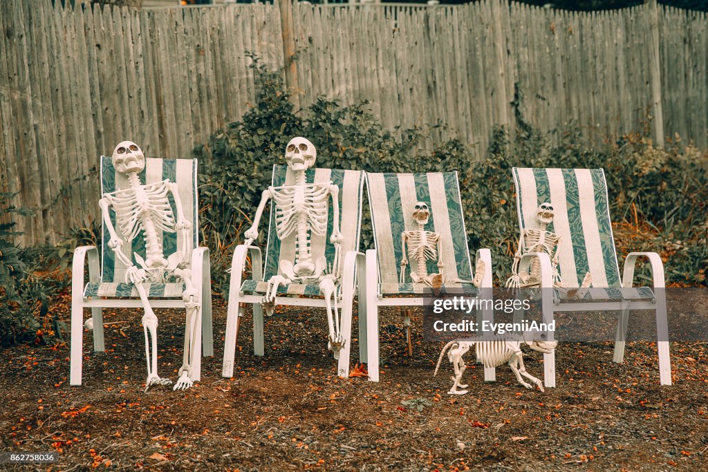 Family of skeletons sits on deck chairs near the house