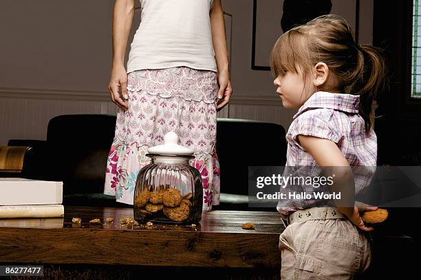 little girl hiding cookie behind her back - colpevolezza foto e immagini stock