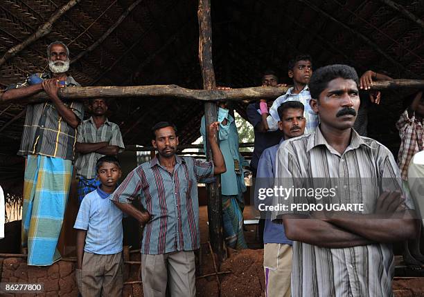 Displaced Tamil civilians watch as unseen British and French foreign ministers David Miliband and Bernard Kouchner arrive at a displaced camp in...