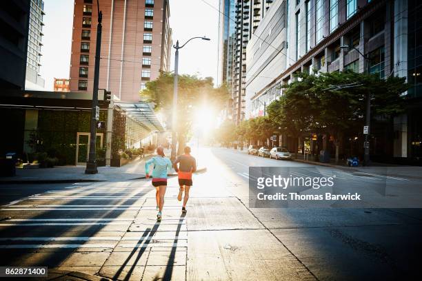 Couple running together on empty city street during workout at sunrise
