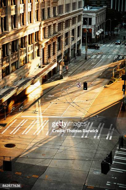 overhead view of man running across crosswalk during early morning run on empty city street - man running city fotografías e imágenes de stock