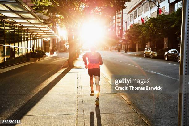 man on early morning run on empty city street - hero images stock-fotos und bilder