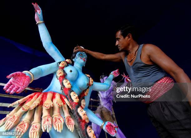 An Indian artist applying colors into the clay idol of goddess Kali at a worship venue on the eve of Kali Puja festival as people offer puja rituals...