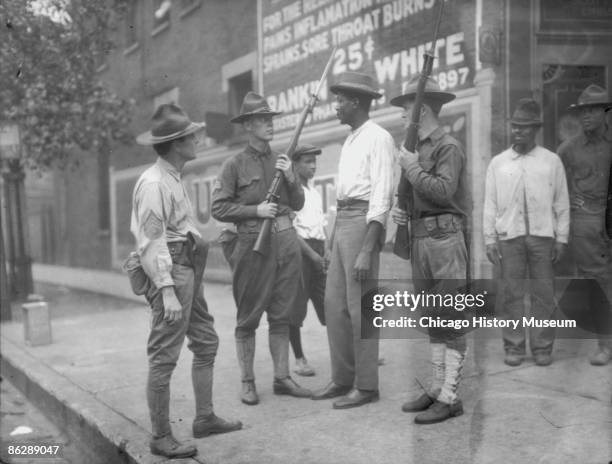 National Guardsmen, called in by Mayor 'Big Bill' Thompson after three days of rioting, question an African American man in Chicago, 1919. The...