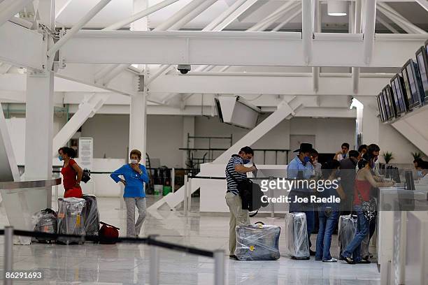 People wear surgical masks to help prevent contracting the swine flu as they check in for the Mexicana airlines flight at the Mexico City...