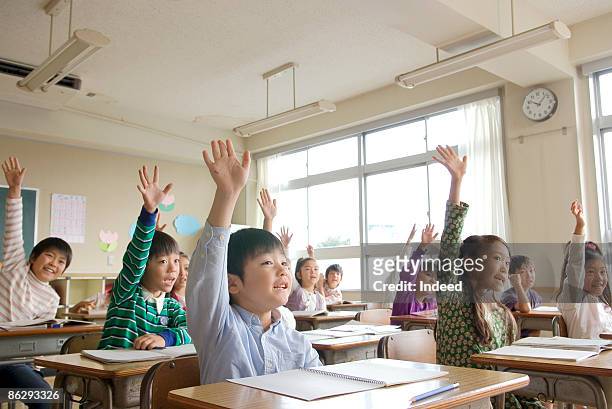 school children raising arms in class - solo bambini foto e immagini stock