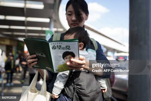 In this picture taken on October 18 a woman carries her baby as she reads an electoral leaflet of Tokyo Governor and leader of the Party of Hope...