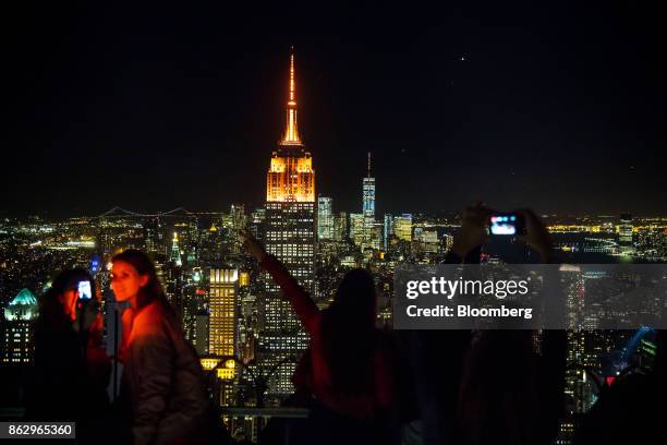 People take photographs as the spires of the Empire State Building, center left, and One World Trade Center, center right, stand lit in orange to...