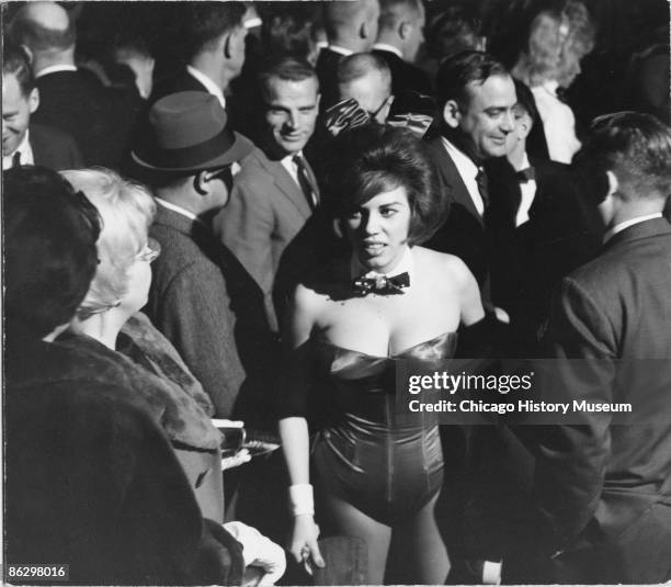 Woman, working as a Playboy bunny, walks through a crowd of men at the Playboy Club, Chicago, ca.1960s.