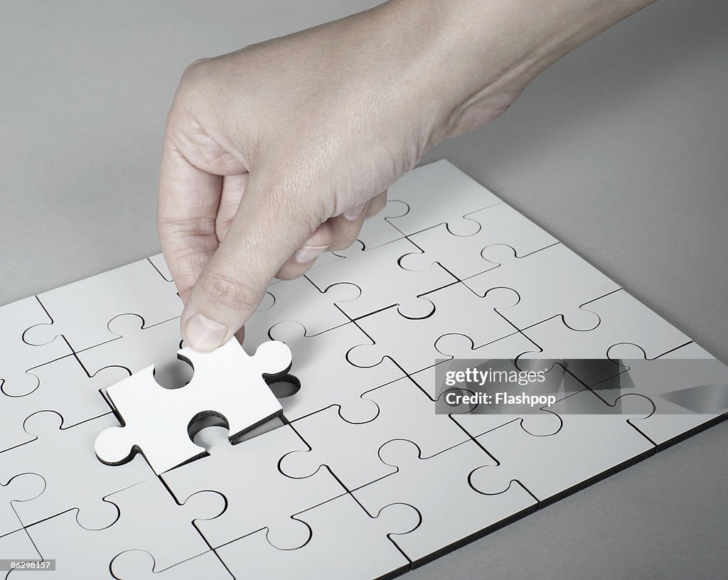 Hand placing last piece into jigsaw puzzle