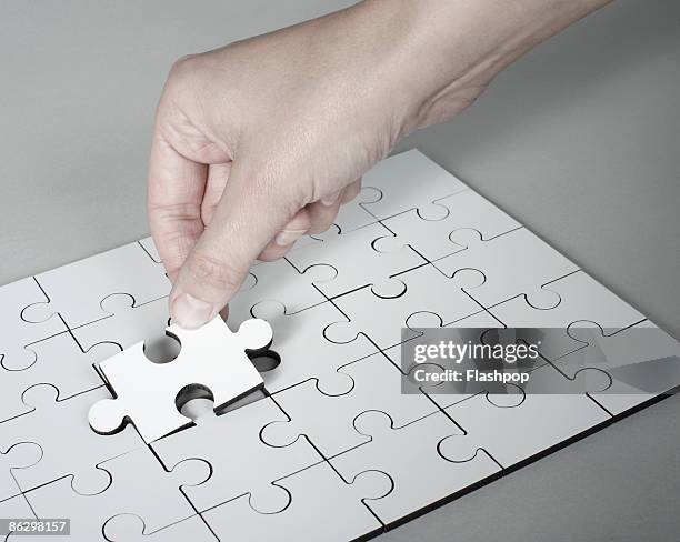 hand placing last piece into jigsaw puzzle - jigsaw stock pictures, royalty-free photos & images