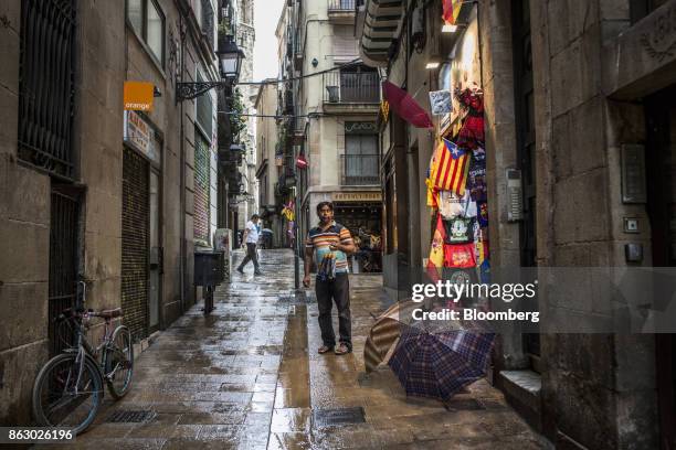 Vendor stands in the street outside his store in an attempt to sell umbrellas to passing pedestrians in Barcelona, Spain, on Thursday, Oct. 19, 2017....