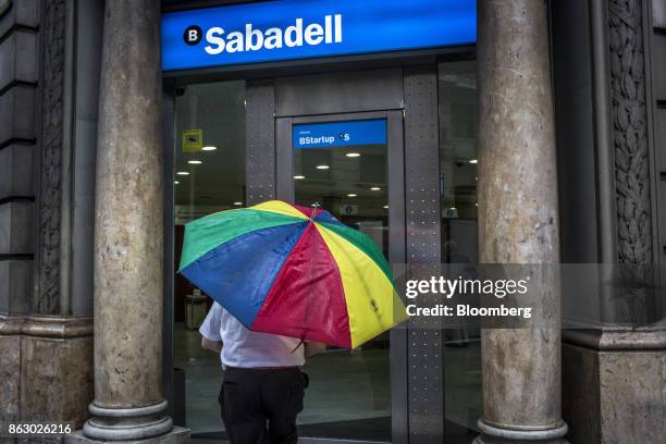 Customer approaches the entrance to a Banco de Sabadell SA bank branch carrying a multicolored umbrella on Via Laietana in Barcelona, Spain, on...