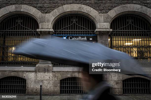Pedestrian carries an umbrella as he passes a CaixaBank SA bank branch on Via Laietana in Barcelona, Spain, on Thursday, Oct. 19, 2017. Spains...