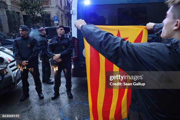 Protesters, including one holding a Catalonian independence flag towards Catalonian riot police, gather in between bouts of pouring rain outside the...