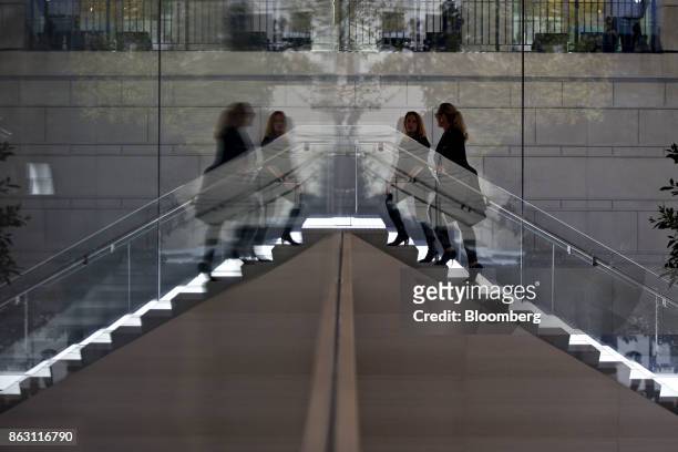 Representatives are reflected in a mirrored wall while climbing a staircase during a media preview of the new Apple Inc. Michigan Avenue store in...