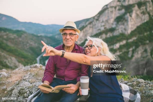 loving senior couple hiking, sitting on the top of rock, exploring. active mature man and woman hugging and happily smiling. - woman sitting top man stock pictures, royalty-free photos & images