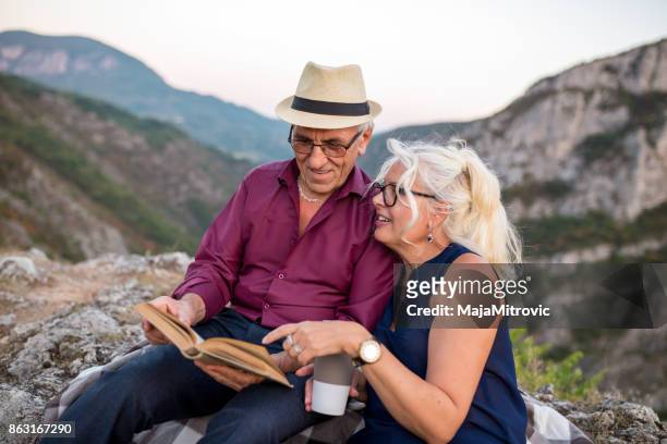 loving senior couple hiking, sitting on the top of rock, exploring. active mature man and woman hugging and happily smiling. - woman sitting top man stock pictures, royalty-free photos & images