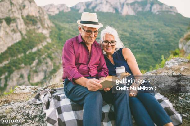 loving senior couple hiking, sitting on the top of rock, exploring. active mature man and woman hugging and happily smiling. - woman sitting top man stock pictures, royalty-free photos & images