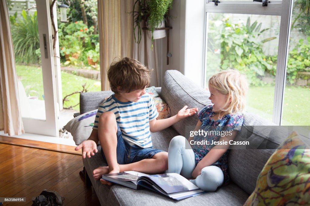 Siblings sitting on sofa looking at book together