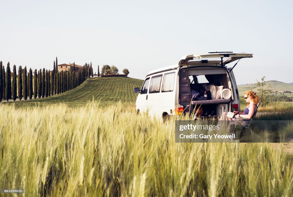 Woman reading a book by campervan in Tuscany landscape