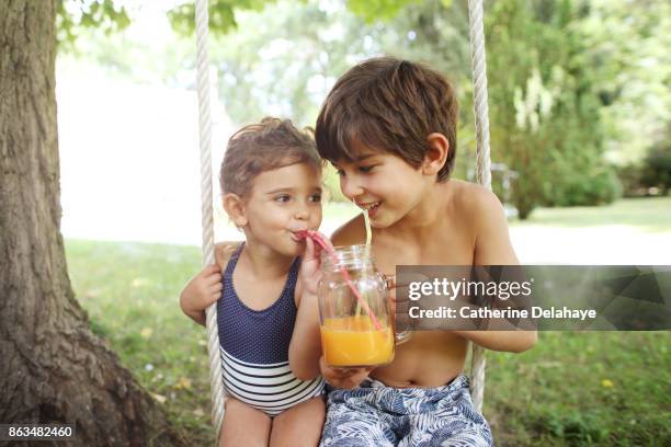 a brother and his sister drinking orange juice seating on a swing - family orange juice photos et images de collection