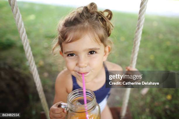 a 3 years old girl drinking orange juice seating on a swing - 2 3 years one girl only ストックフォトと画像