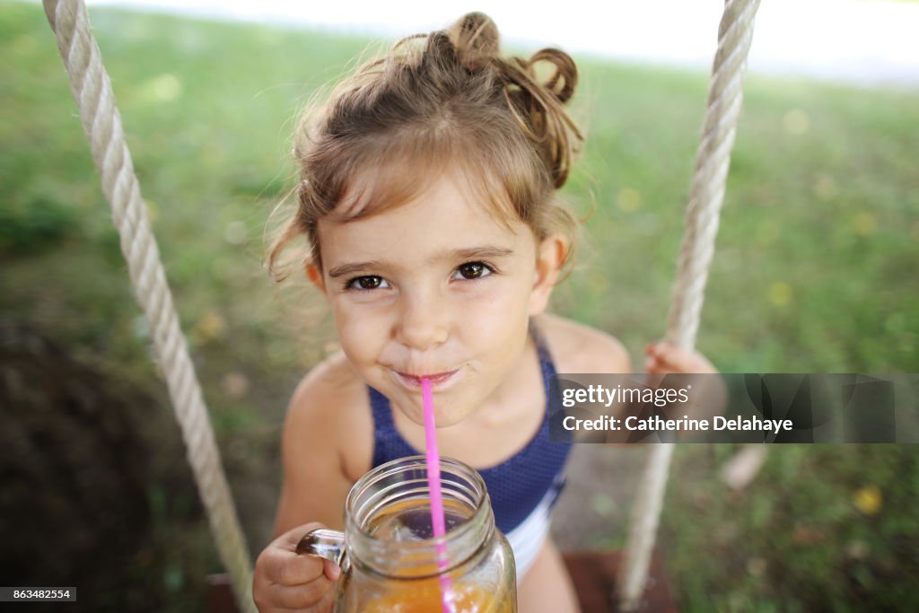 A 3 years old girl drinking orange juice seating on a swing