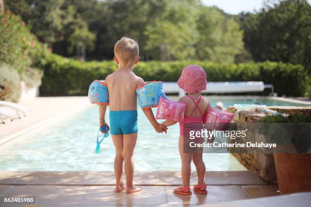 2 children with water wings by the swimming pool - boy swimming pool goggle and cap stock pictures, royalty-free photos & images