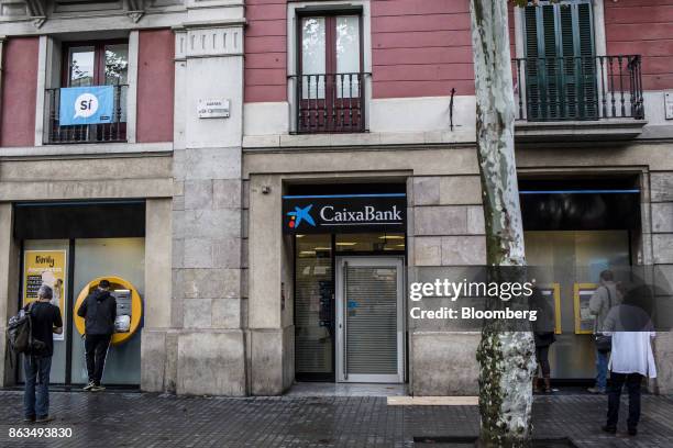 Customers queue to withdraw cash from an automated teller machine outside a CaixaBank SA bank branch in Barcelona, Spain, on Friday, Oct. 20, 2017....