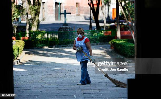 Women wears a surgical mask to help prevent contamination with the swine flu as she sweeps a courtyard May 2, 2009 in Mexico City, Mexico. The...
