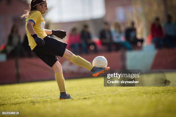 full length of female goalkeeper kicking soccer ball on playing field. - soccer goalkeeper stock pictures, royalty-free photos & images