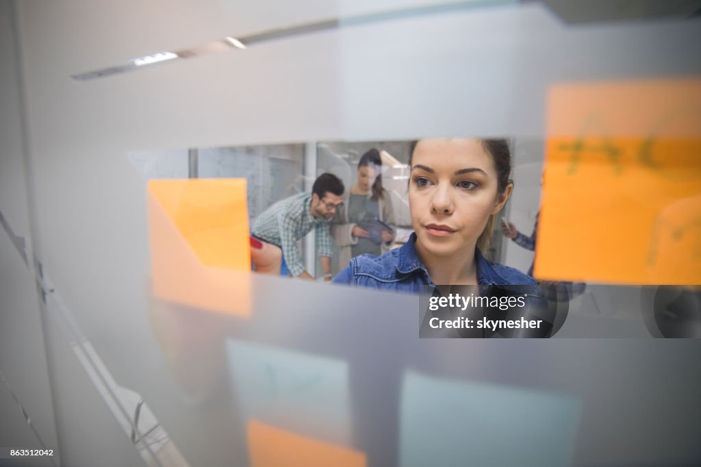 Young businesswoman writing business plan on adhesive notes in the office.