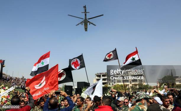 Syrians wave their national flags and those of the Syrian Social Nationalist Party in a stadium as a Russian-made Mil Mi-24 helicopter gunship hovers...